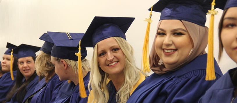 a group of graduates stand in a line wearing their caps and gowns, smiling